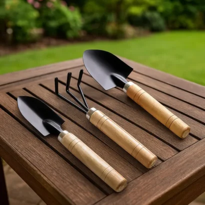 Three-piece garden tool kit with wooden handles including a hand trowel, cultivator, and transplanter placed on a gardening surface.