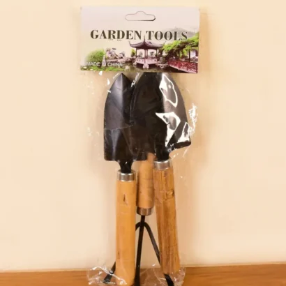 Close-up view of a hand trowel, cultivator, and transplanter with strong wooden handles placed on garden soil.